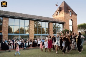 At Les Ecuries de la Tour in Mondonville, the bride tosses her bouquet as all the young women at the wedding eagerly rush to catch it on the lawn outside, capturing a lively and joyous moment.